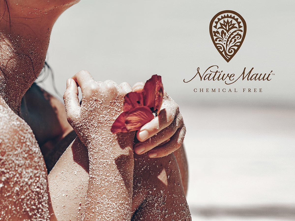 Native Maui lifestyle image of sand-covered shoulders holding a red flower