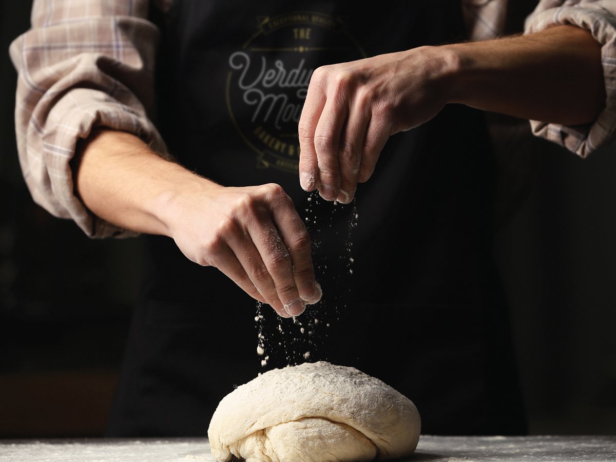 Baker dusting flour over fresh dough at The Verdugo Mountain Bakery